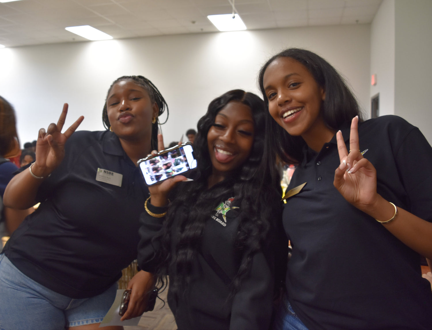 Three women posing together in a room with a camera and phone.