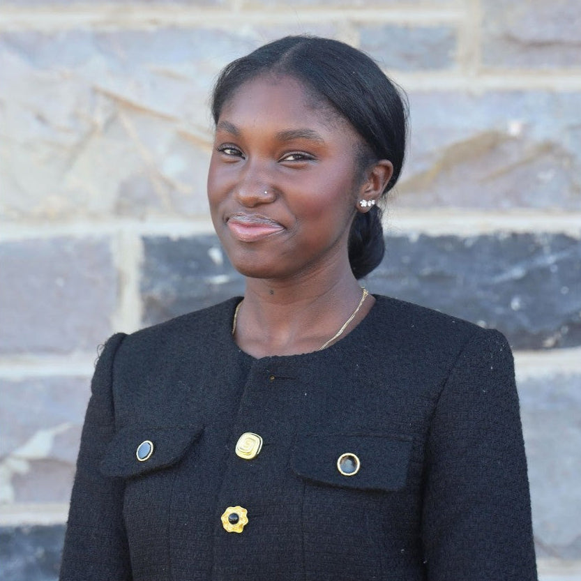 Woman wearing a black coat with gold buttons against a stone wall background